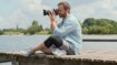 En fotograf sidder på en mole og tager billeder. Han har en knæskinne på.