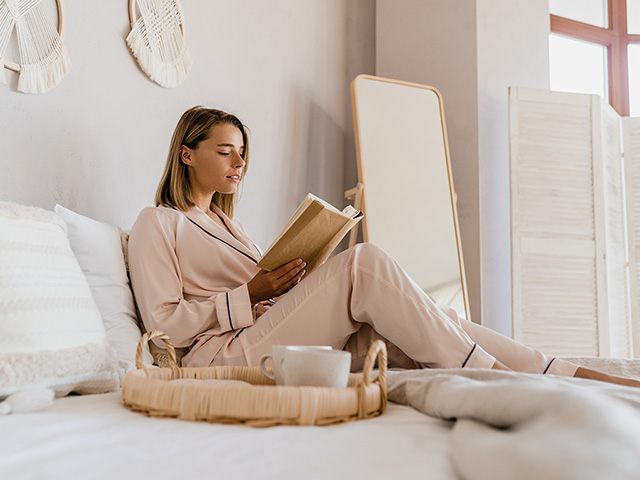 Frau sitzt auf dem Bett und liest ein Buch