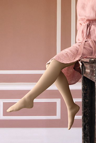 2. Imagen de estilo de vida Juzo Soft Mujer con Juzo Soft Sesame sentada en una repisa de chimenea