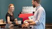 Empregada de mesa a usar o pulso elástico JuzoFlex Manu Xtra e entrega aos clientes uma chávena sobre o balcão