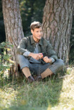 Man wearing Juzo Adventure, sitting under a tree and cutting an apple