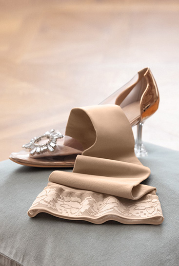 3. Imagen de estilo de vida Juzo Soft Juzo Soft Sesame tumbado en un cojín junto a un zapato de Cenicienta