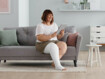 Eine Frau sitzt auf der Couch, liest am Tablet und trägt am Bein den Juzo SoftCompress