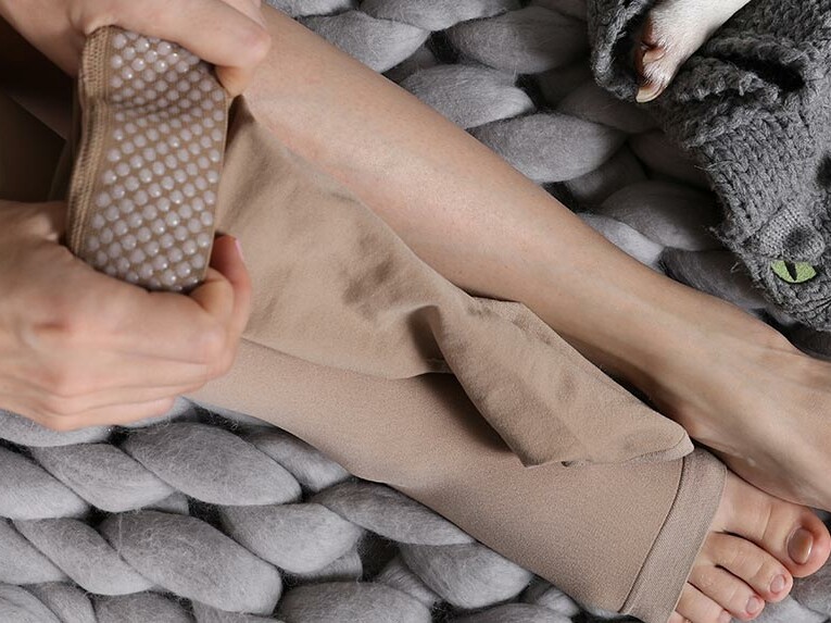 Eine Frau zieht ihre Kompressionsversorgung an und sitzt dabei auf einer kuscheligen Decke