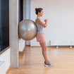 A woman leaning upright against a wall with an exercise ball