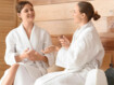zwei Frauen sitzen im Bademantel in der Sauna und unterhalten sich