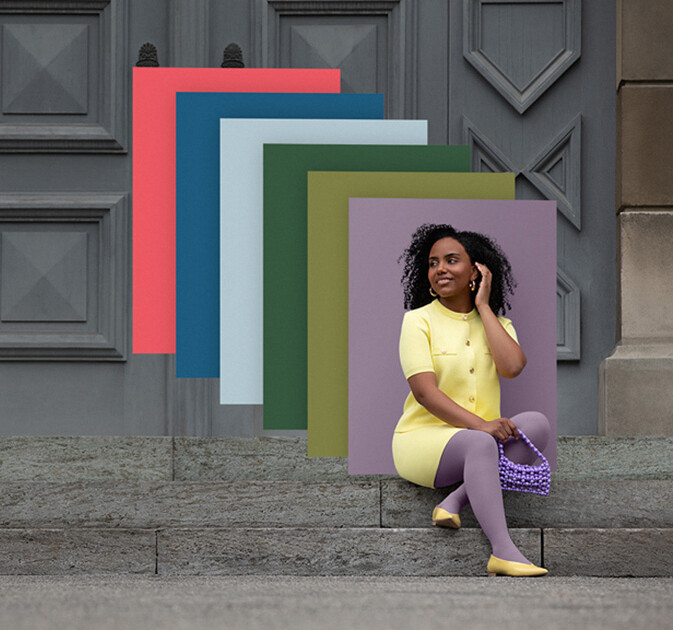 Juzo Trend Colours Batik Una donna siede di fronte a un muro fiorito. Indossa un trattamento compressivo in colore giallo con motivo Batik bianco