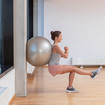 A woman leaning against a wall with an exercise ball, doing a squat with one leg extended